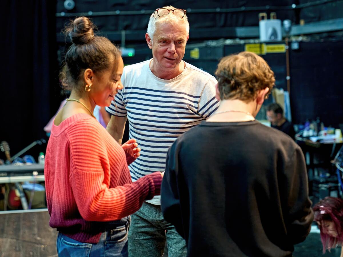 A stage director talks to two young actors during rehearsal.