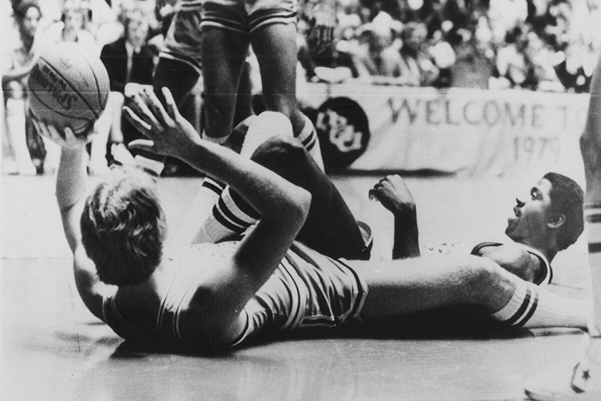 Larry Bird  and Magic Johnson lie on the floor of the court.