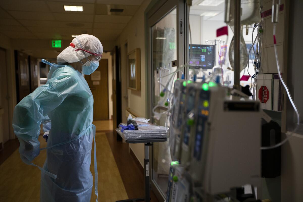 A nurse in protective gear ties an isolation gown around herself in an ICU hall.