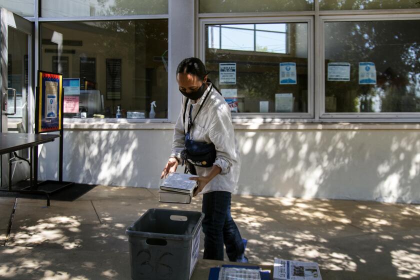 LOS FELIZ, CA - SEPTEMBER 24, 2020: Bronwen Serna of Los Angeles drops off library books to a tub outside the Los Feliz branch of the Los Angeles Public Library during the coronavirus pandemic on September 24, 2020 in Los Feliz, California. This library is a "library to go" where residents can requests books and then set up a reservation time to pick them up outside the library.(Gina Ferazzi / Los Angeles Times)