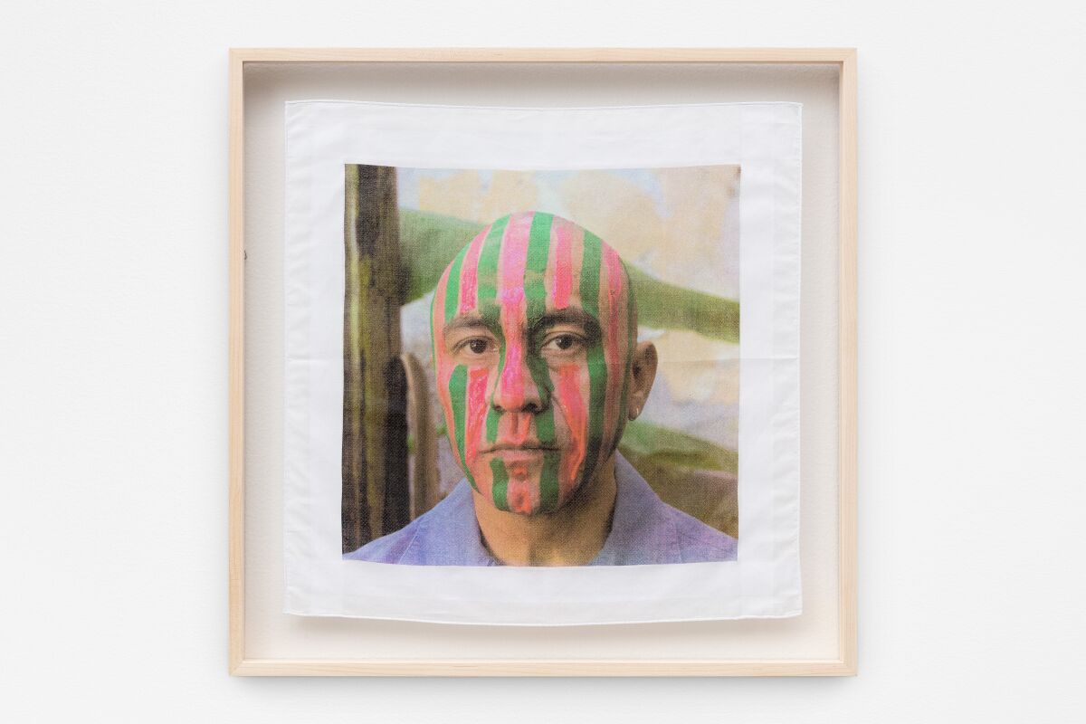 A framed photo of a bald man with pink and green vertical stripes painted on his face 