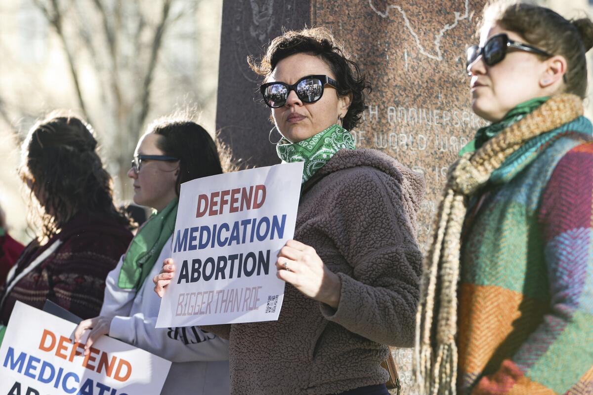 Women hold protest signs in support of access to abortion medication.