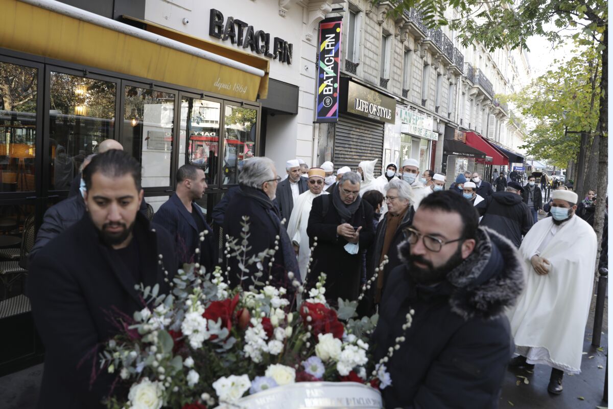 Members of the muslim community carry a bouquet of flowers before paying their homage to the victims of the Nov.13, 2015 attacks, outside the Bataclan concert hall in Paris, Friday, Nov.12, 2021 on the eve of the sixth anniversary of the attacks. Fourteen men are currently on trial over the Nov. 13, 2015, Islamic State attacks in Paris that killed 130 people. (AP Photo/Adrienne Surprenant)