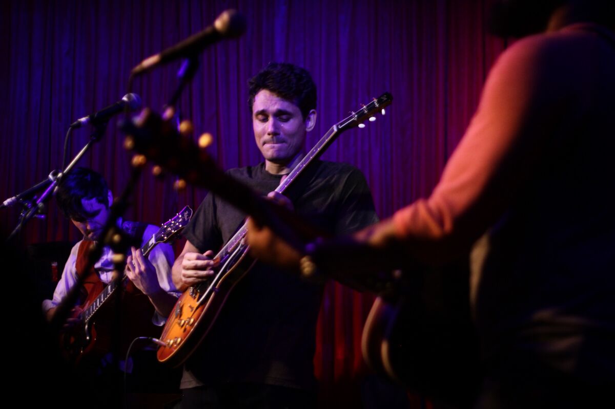 John Mayer, among other performers, plays a guitar onstage.