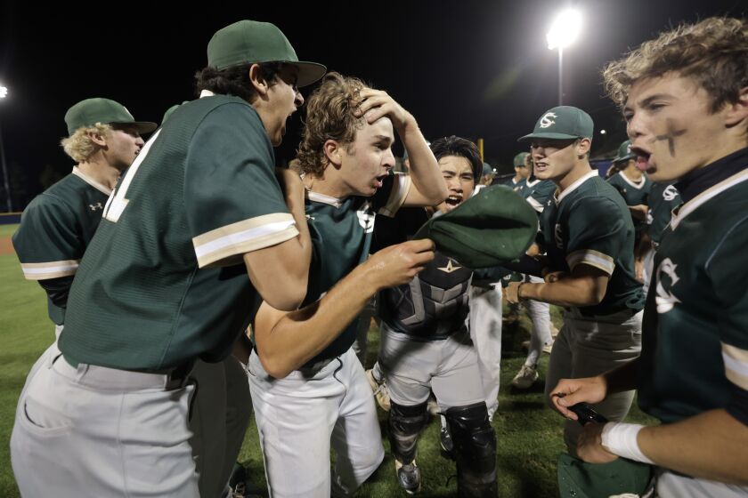 Sage Creek pitcher Luke Caruso puts his hand on his forehead as teammates swarm him while they celebrate Sage Creek's 5-0 win over Cathedral Catholic to take the CIF San Diego Section Division II baseball championship at Fowler Park in San Diego on Thursday, May 25, 2023.
