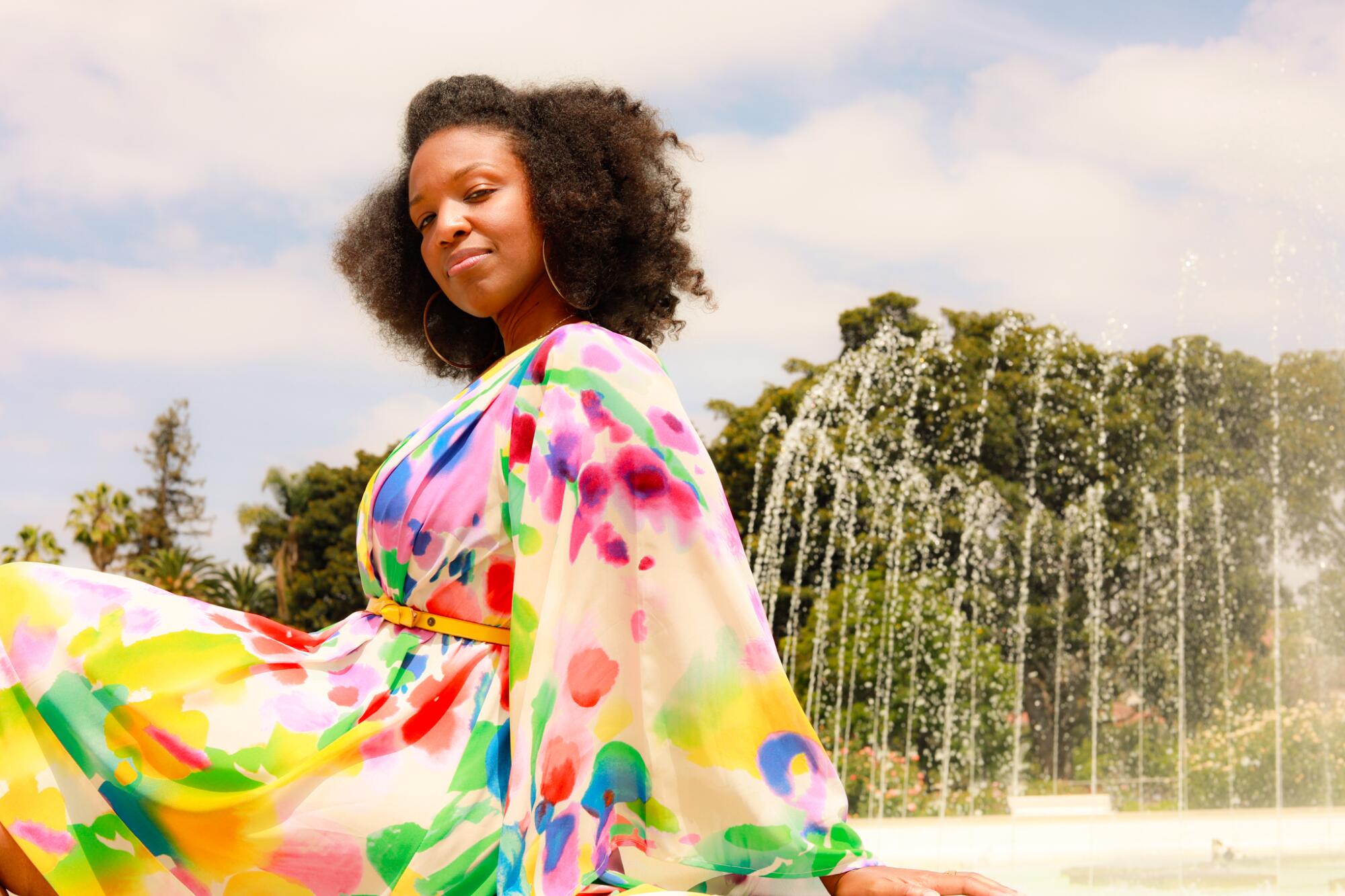 A woman in a flowery dress sits next to a fountain.