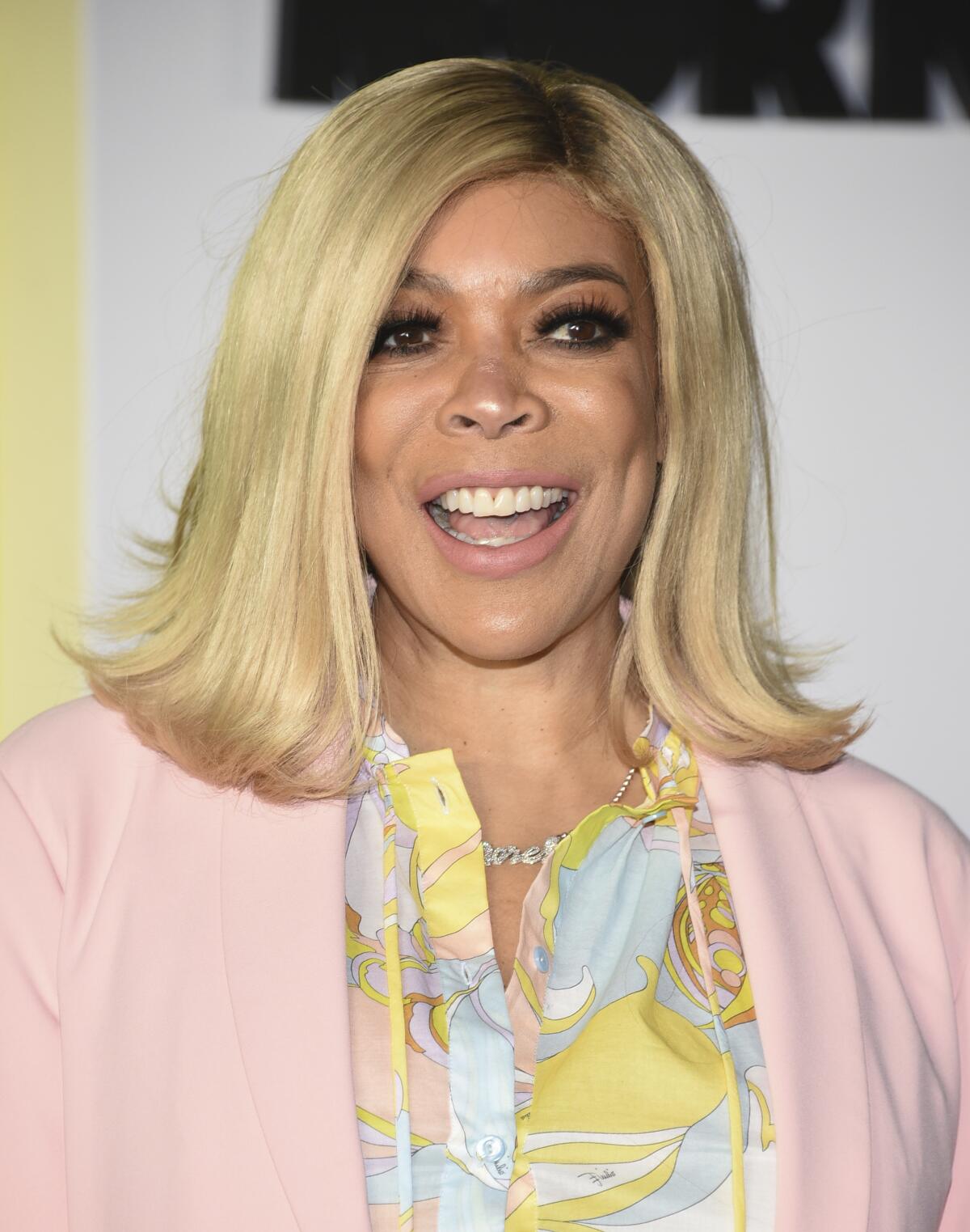 Wendy Williams smiling in a colorful shirt and pink jacket