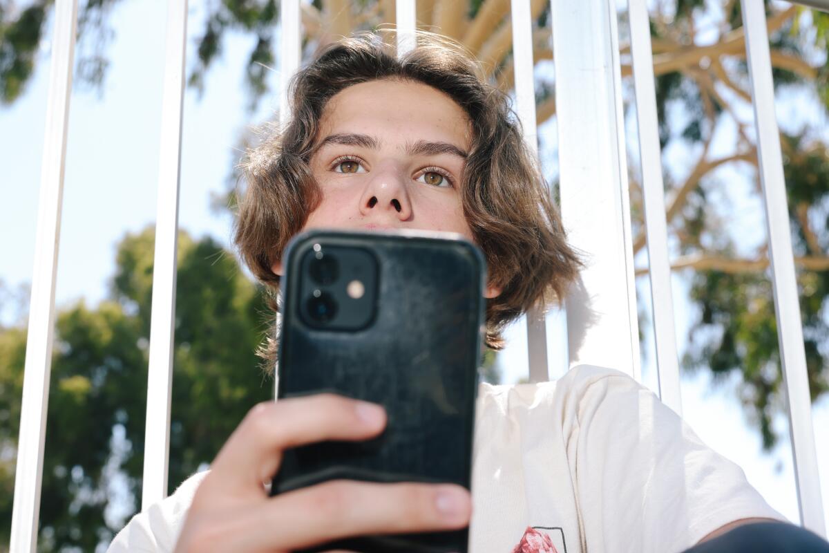 A teenage boy hold a cell phone in front of his face. 