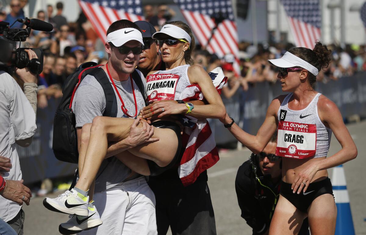 Steve Edwards carries his wife, Shalane Flanagan, after she fell to the ground in exhaustion following her third-place finish in the U.S. Olympic women's marathon trial on Saturday. Training partner Amy Cragg, who won the race, was the first to arrive at her side as Flanagan crossed the finish line.