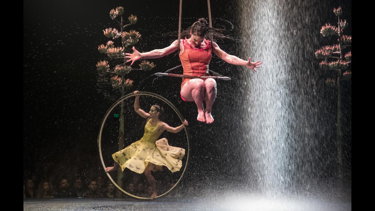 Trapeze artist Enya White, drenched by rainfall, whips through the air while Angelica Bongiovonni spins in a Cyr wheel.