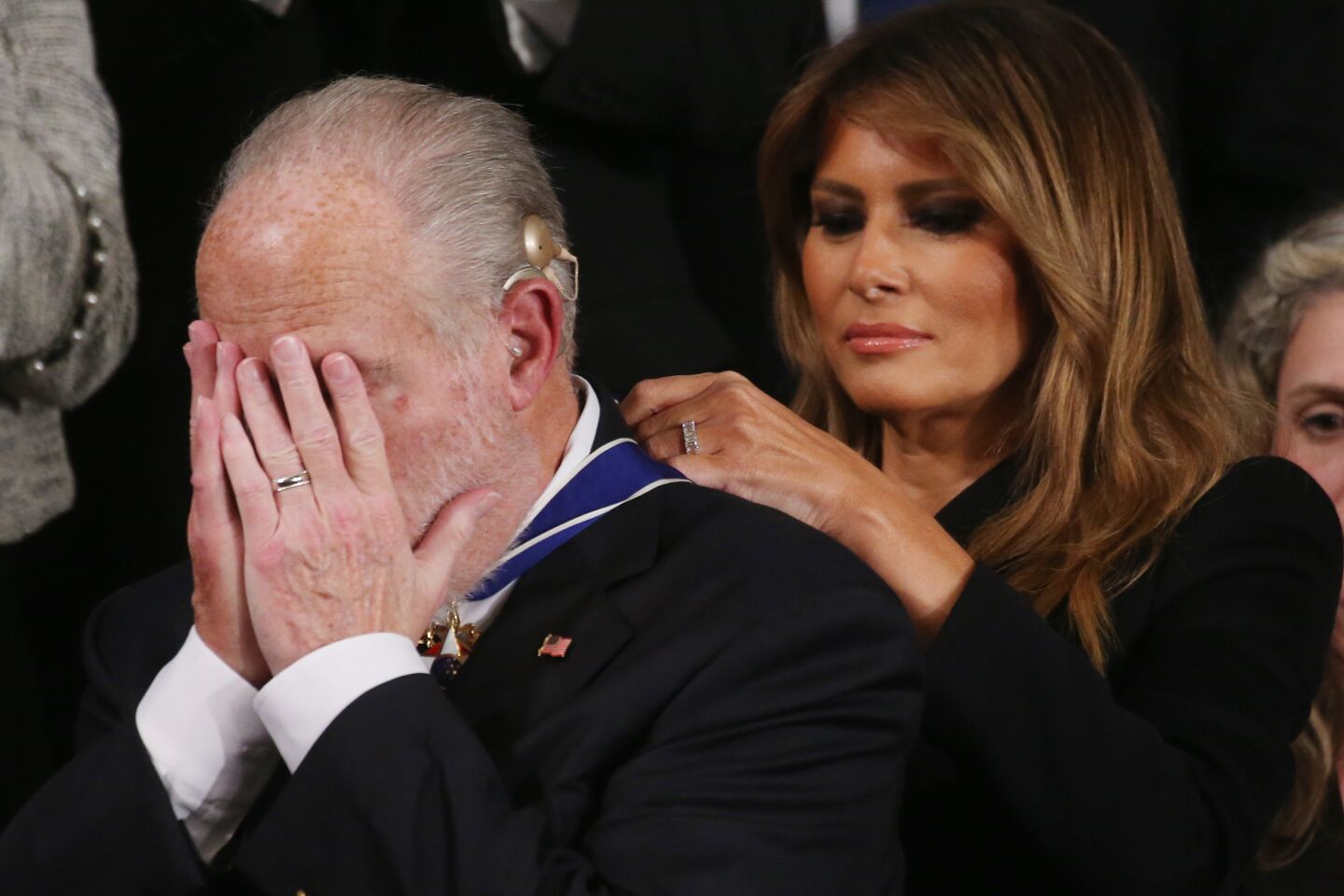 Melania Trump puts the medal around Limbaugh's neck as he covers his face with both hands.