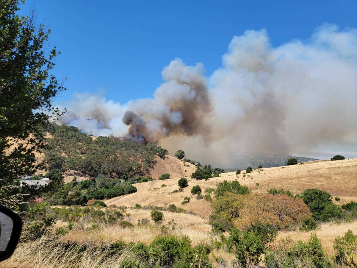 Smoke rises from a fire on brush-covered hillsides.