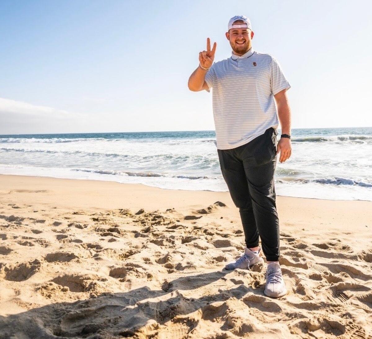 Cooper Lovelace makes the peace sign, or USC victory sign, with his fingers as he stands on a beach.