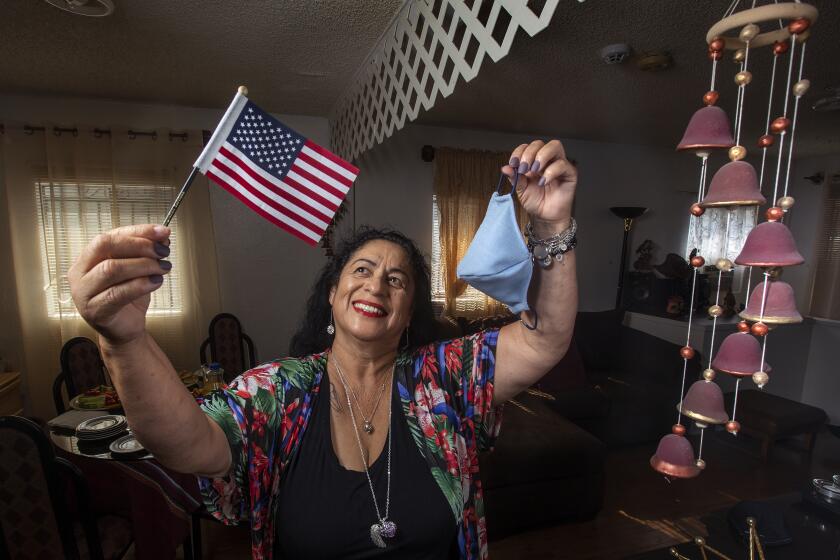 LOS ANGELES, CA -SEPTEMBER 18, 2020: Clemencia Morales, who comes from Guatemala and became a U.S. citizen on August 20, 2020, the day after her 65th birthday, is photographed at her home in Los Angeles. In one hand she is holding the American flag that was given to her when she took the oath to become a U.S. citizen at the Federal Building in downtown Los Angeles. In the other hand she is holding one of the over 5000 masks she made from fabric she had around the house and handed out for free to people in Compton as they were standing in line for food. At right is a pottery chime from Guatemala. (Mel Melcon / Los Angeles Times)