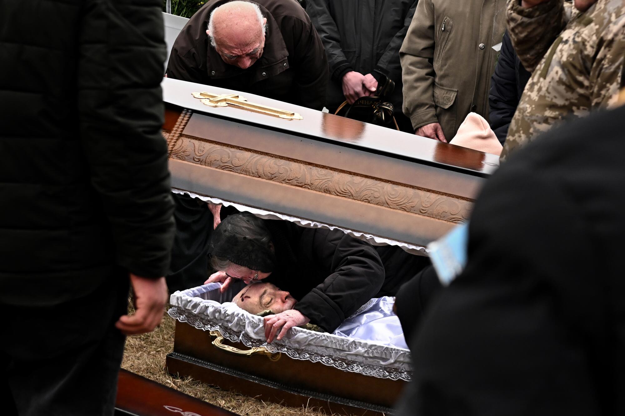 A woman kisses a body in a coffin surrounded by people.