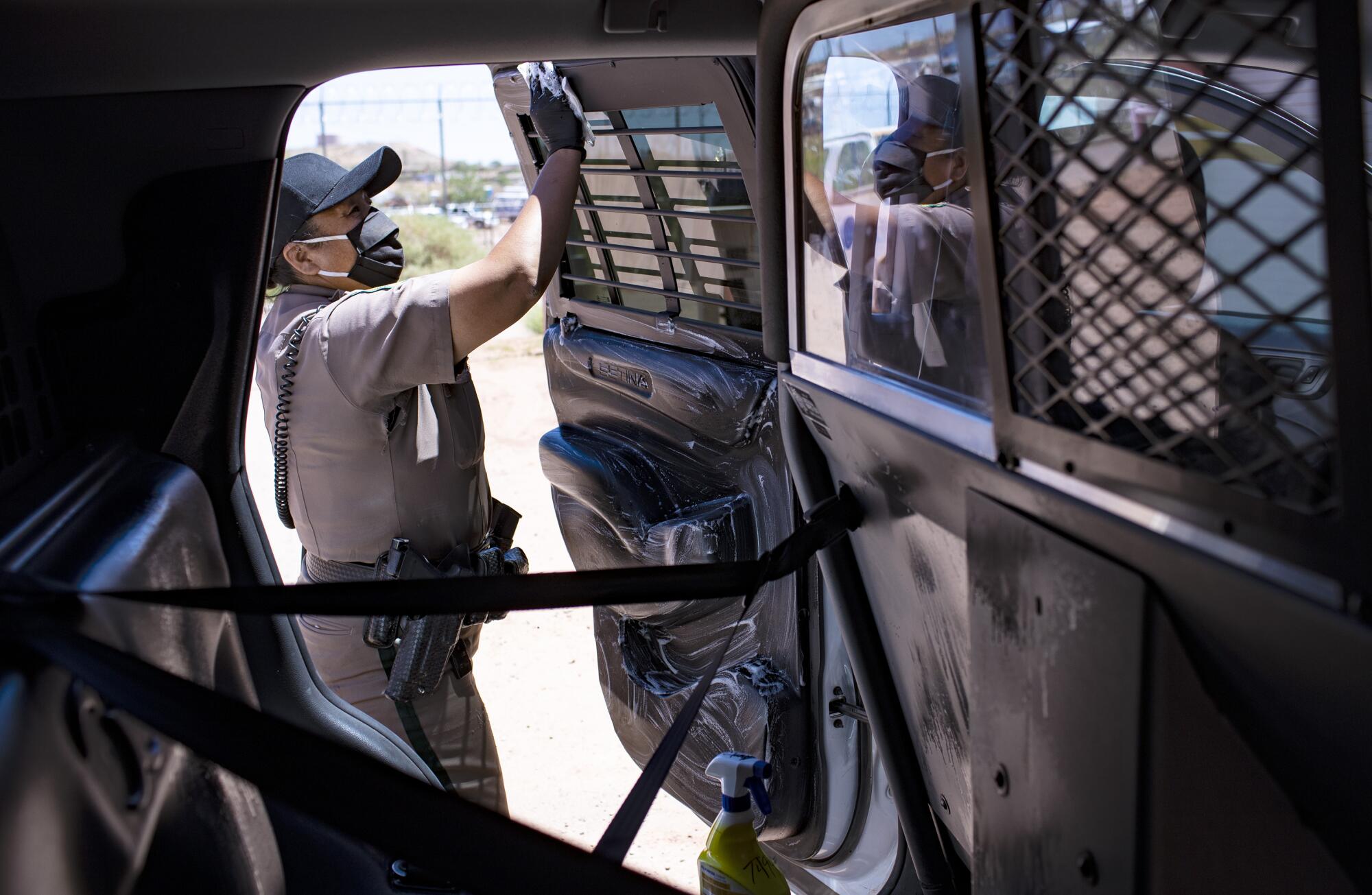 Officer Carolyn Tallsalt disinfects the back of her police vehicle after transporting a man to jail