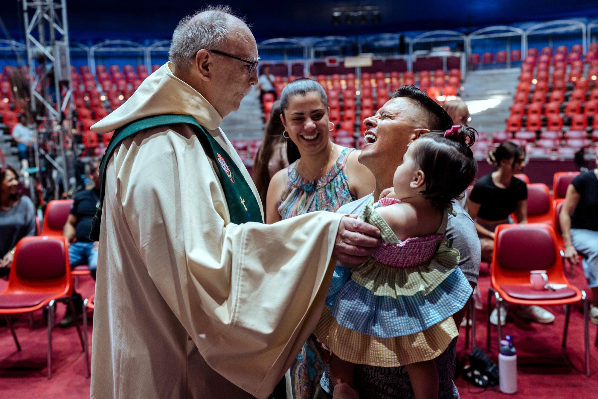 Father Frank Cancro speaks with Daniel Eguino, holding Natasha, and Thatiana Fischer.