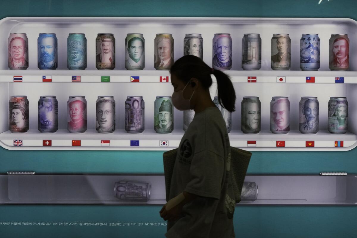 A woman walks past a sign advertising a bank's currency exchange rates in Seoul