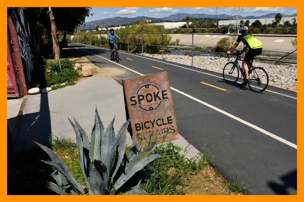 Two cyclists going in opposite directions use the path along the Los Angeles River. A sign beside plants reads "Spoke."