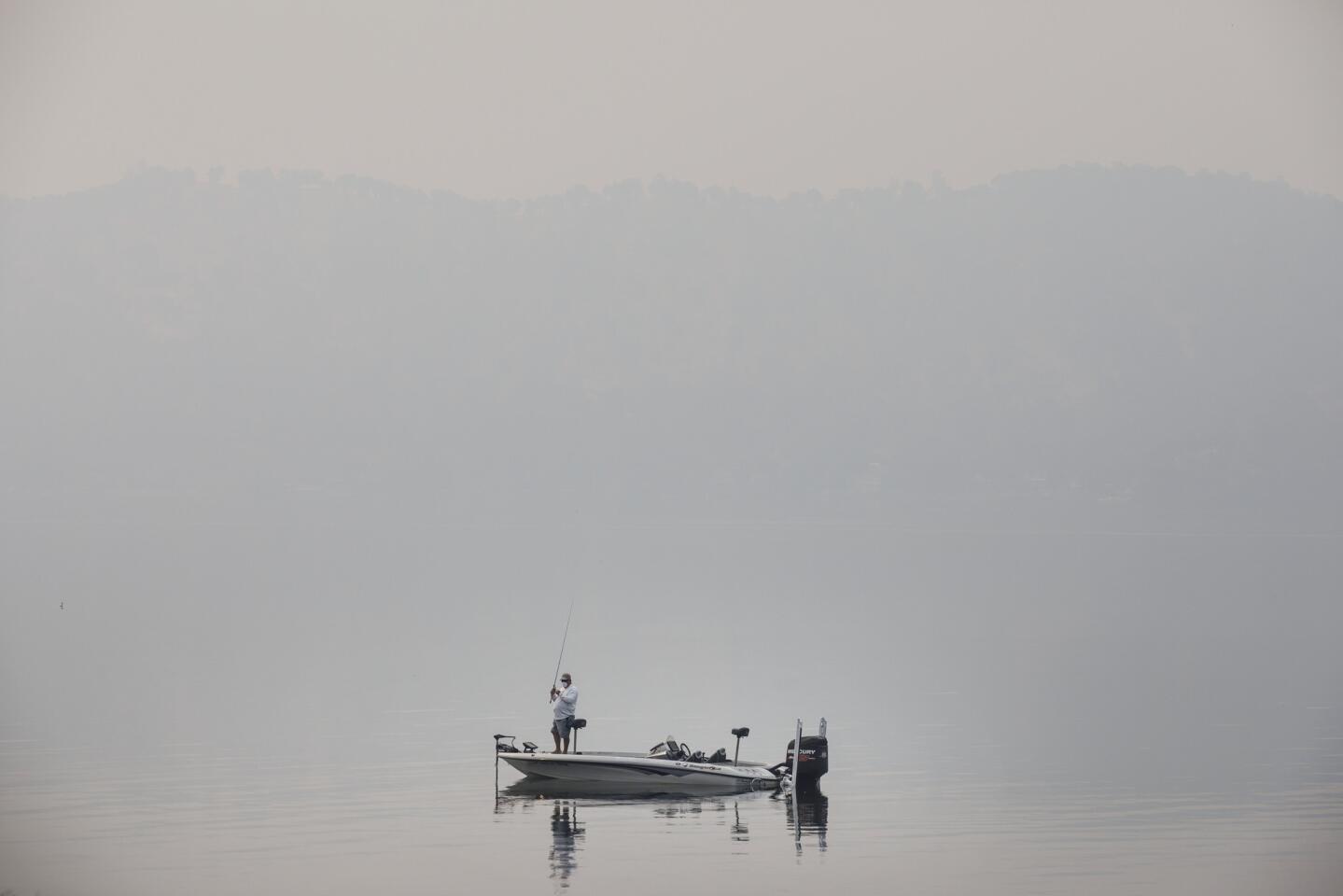 A fisherman wears a mask while fishing from his boat as smoke from the Mendocino Complex fire covers Clear Lake, on Aug. 8, 2018.