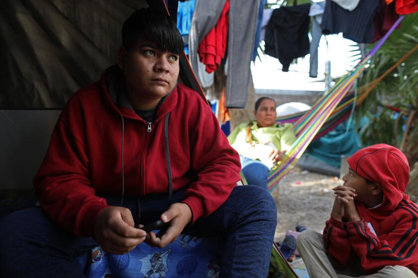 MATAMOROS, TAMAULIPAS -- TUESDAY, DECEMBER 3, 2019: Steven Solis Campos, 15, left, of El Salvador, who has varicella or chicken pox, shown with his mother Ana Patricia Campos Pineda, right, at a migrant encampment near the bank of the Rio Grande in Matamoros, Mexico. Steven and his mother were both turned away back to Mexico by U.S. Customs and Border Protection, not being allowed to be present at their asylum court hearing on Dec. 2, 2019, because Steven has varicella. They were rescheduled for Feb. 20, 2020. Asylum seeking migrants and their children are being illegally turned away from Remain in Mexico hearings on the border, including at temporary immigration tent courts, for being sick. Migrants from Central America and Mexico await the outcome of their U.S. immigration court cases in a tent encampment, home to more than 2,500 people, near the Gateway International Bridge at the U.S.-Mexico border in Matamoros, Tamaulipas, on Dec. 3, 2019. The stranded migrants seeking political asylum remain in Mexico under Trump administration’s “Remain in Mexico” policy. (Gary Coronado / Los Angeles Times)