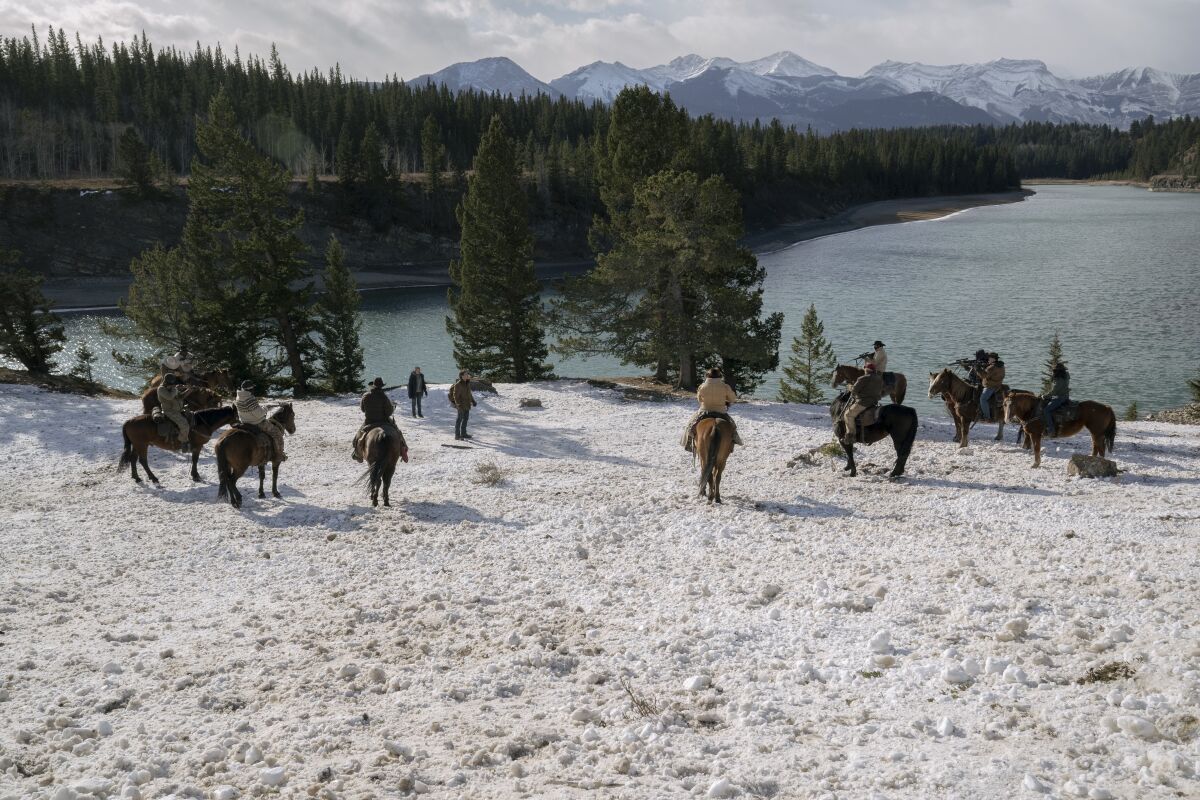 People on horseback in a snowy clearing, with mountains and trees in the distance.