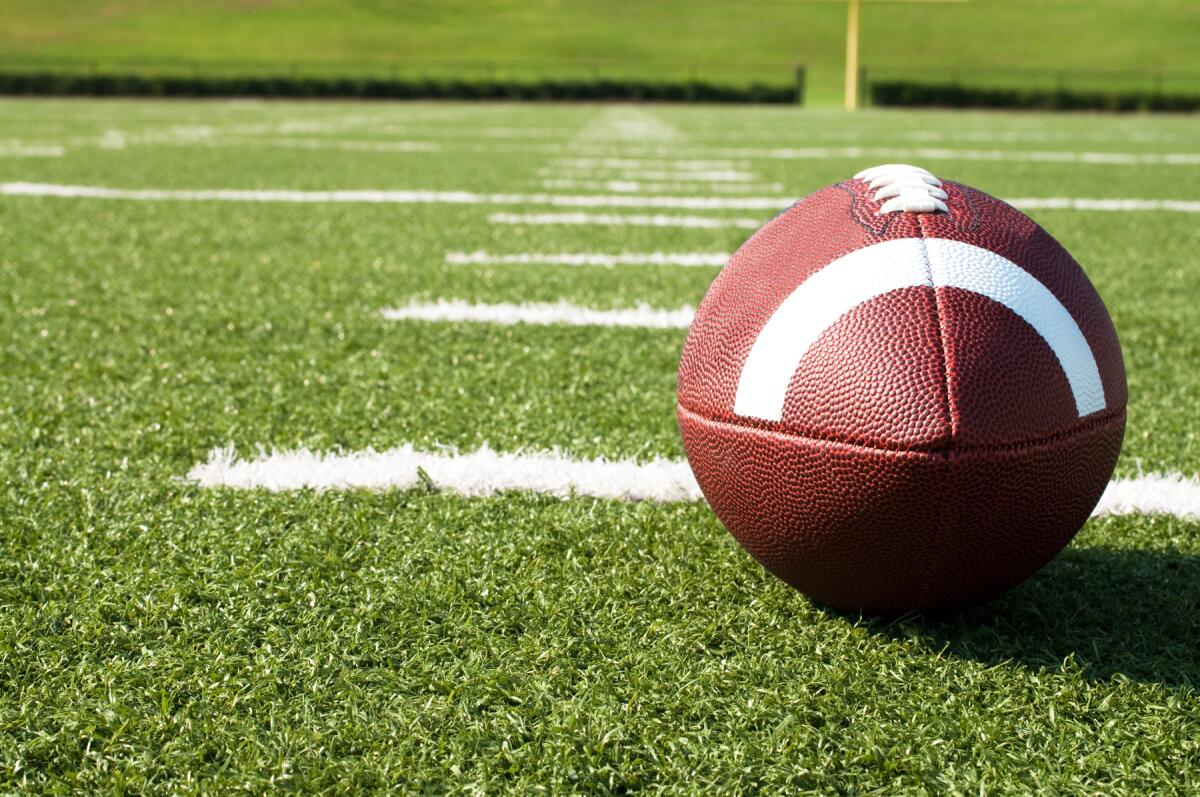 Closeup of American football on field with yard lines.