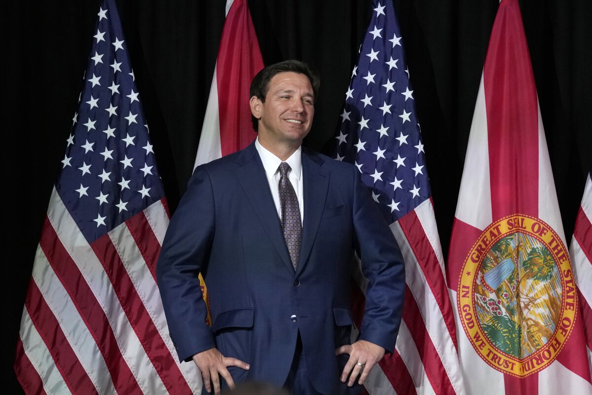 Florida Gov. Ron DeSantis stands with flags behind him 