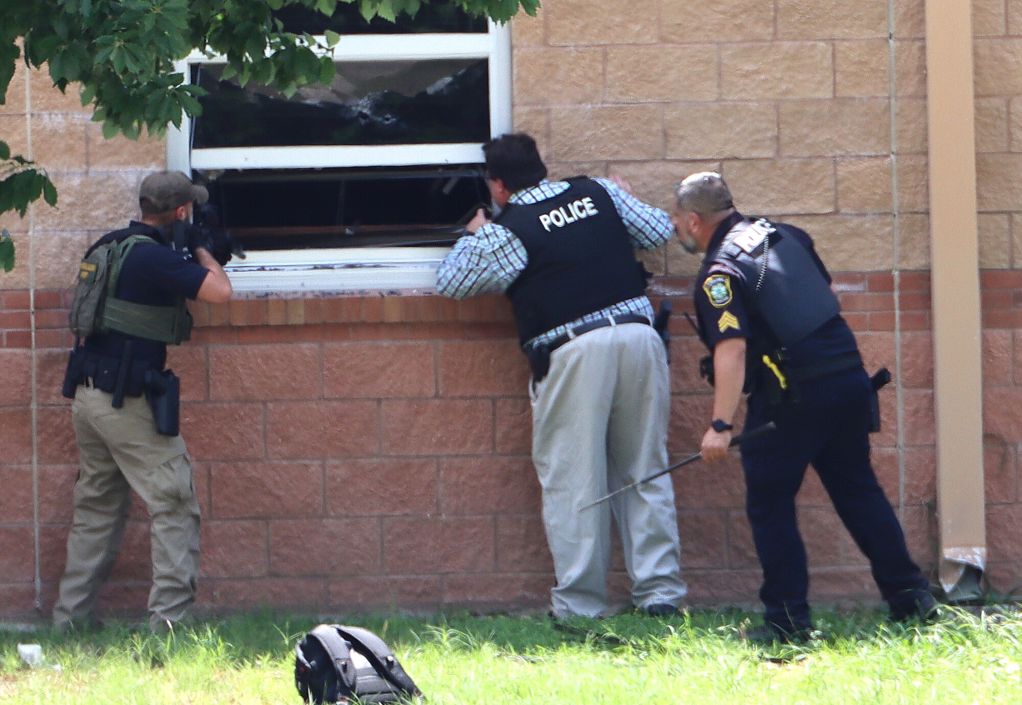 Police with guns drawn peer in a window at Robb Elementary School on the day of the shooting.
