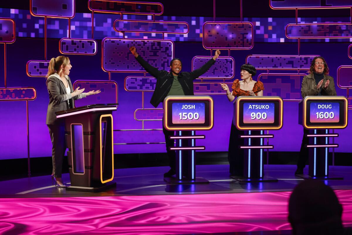 Game show panel with a host and three contestants with a purple screen in back.