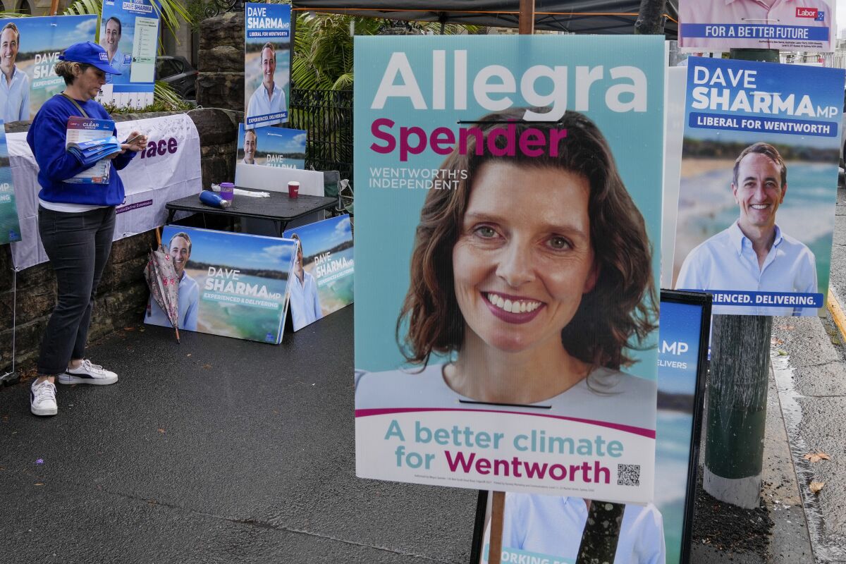 A volunteer stands amongst billboards for independent candidate Allegra Spender and incumbent Liberal candidate Dave Sharma outside a polling booth in Sydney, Australia on May 9, 2022. Sydney businesswoman Spender has an impeccable pedigree for a career in Australian politics. She is the daughter of a conservative federal lawmaker and granddaughter of a conservative cabinet minister. More surprising than her decision to run for office, she has chosen to become a candidate of a breakaway political grouping that has emerged as a threat to the ruling conservative Liberal Party. (AP Photo/Mark Baker)