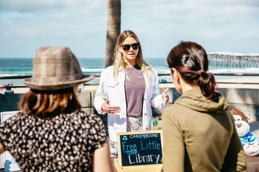 Trisha Goolsby, Pacific Beach Boardwalk'ta yoldan geçenlerle Cans4Books Topluluk Girişimi hakkında konuşuyor.