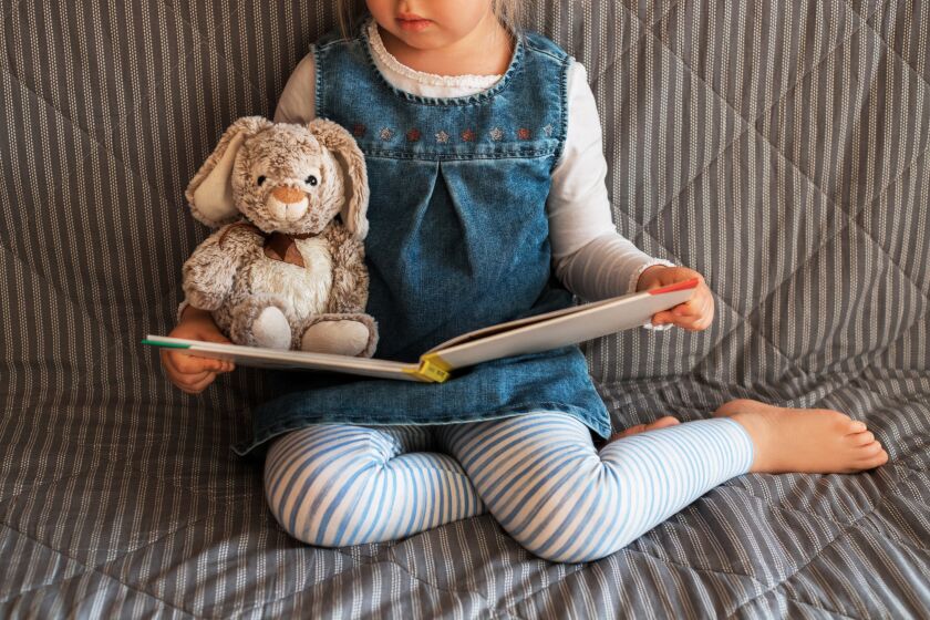 Little girl reading a book with her toy rabbit.