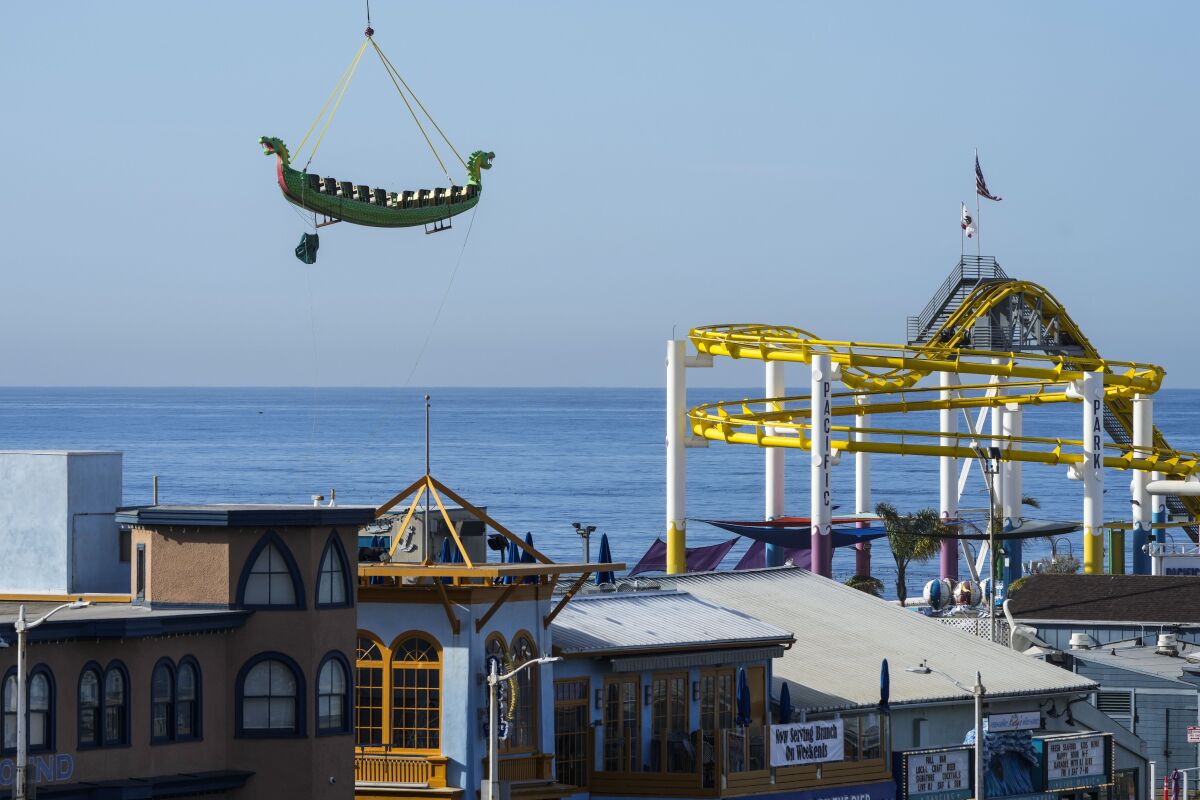 A swinging ship ride is lifted up by a helicopter over the Santa Monica Pier.