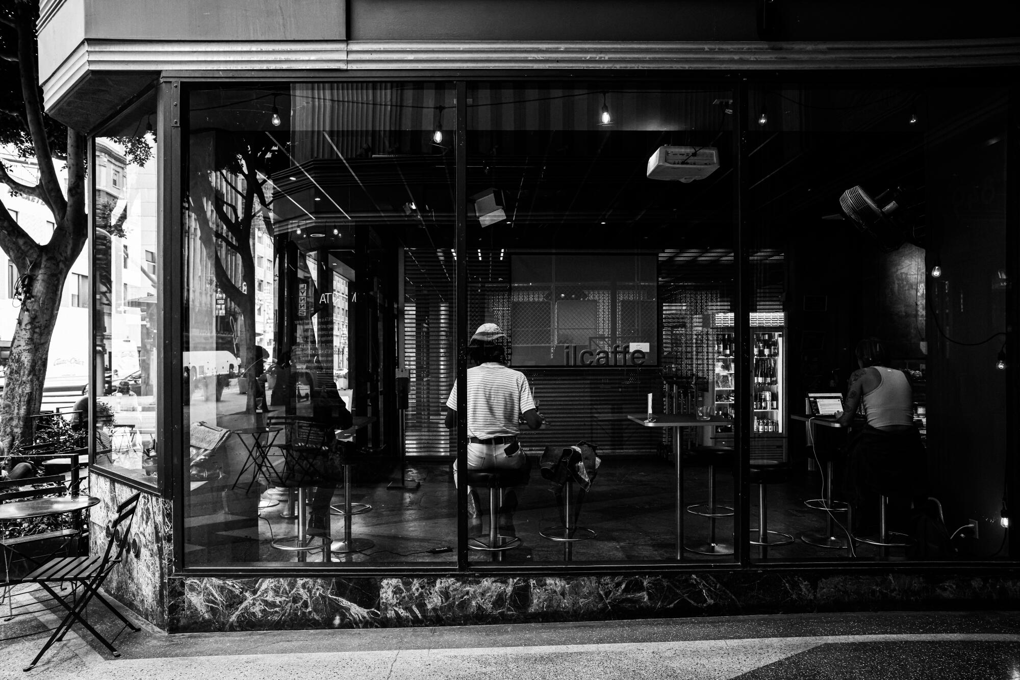 Patrons sit at barstool tables, as seen from outside a window