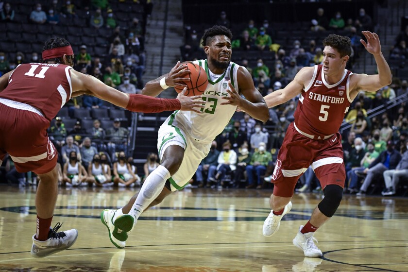 Oregon forward Quincy Guerrier (13) drives to the basket while guarded by Stanford forward Jaiden Delaire (11) and guard Michael O'Connell (5) during the first half of an NCAA college basketball game Thursday, Feb. 10, 2022, in Eugene, Ore. (AP Photo/Andy Nelson)