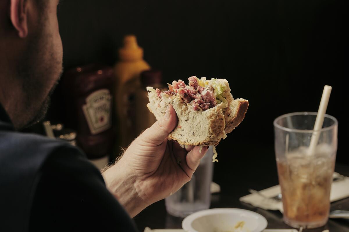 A hand holds up half of a deli sandwich