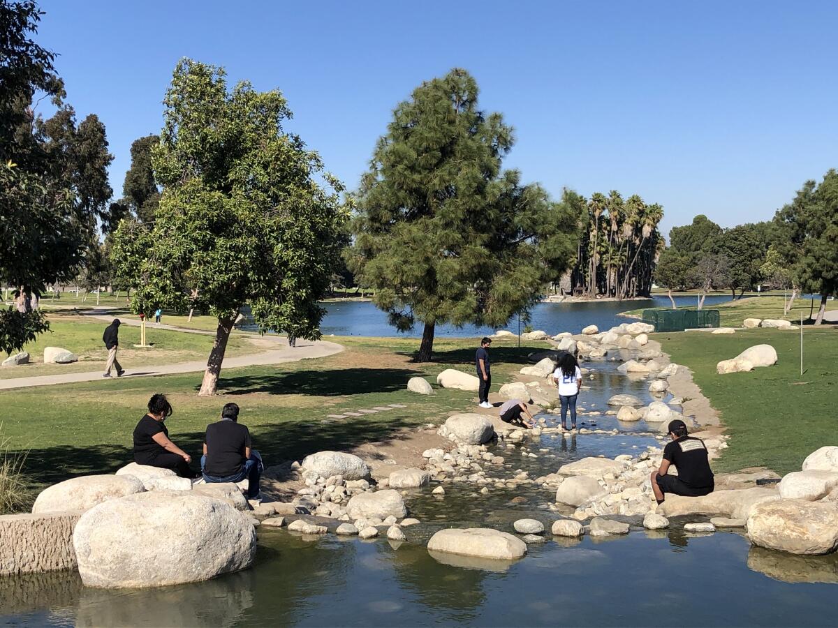 Park patrons sit on rocks and boulders in a set of shallows that connect two lakes.