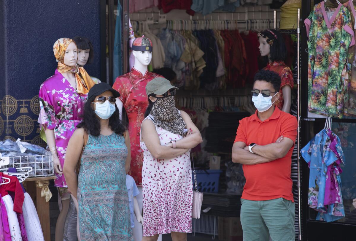 People wearing masks stand outside a clothing store.