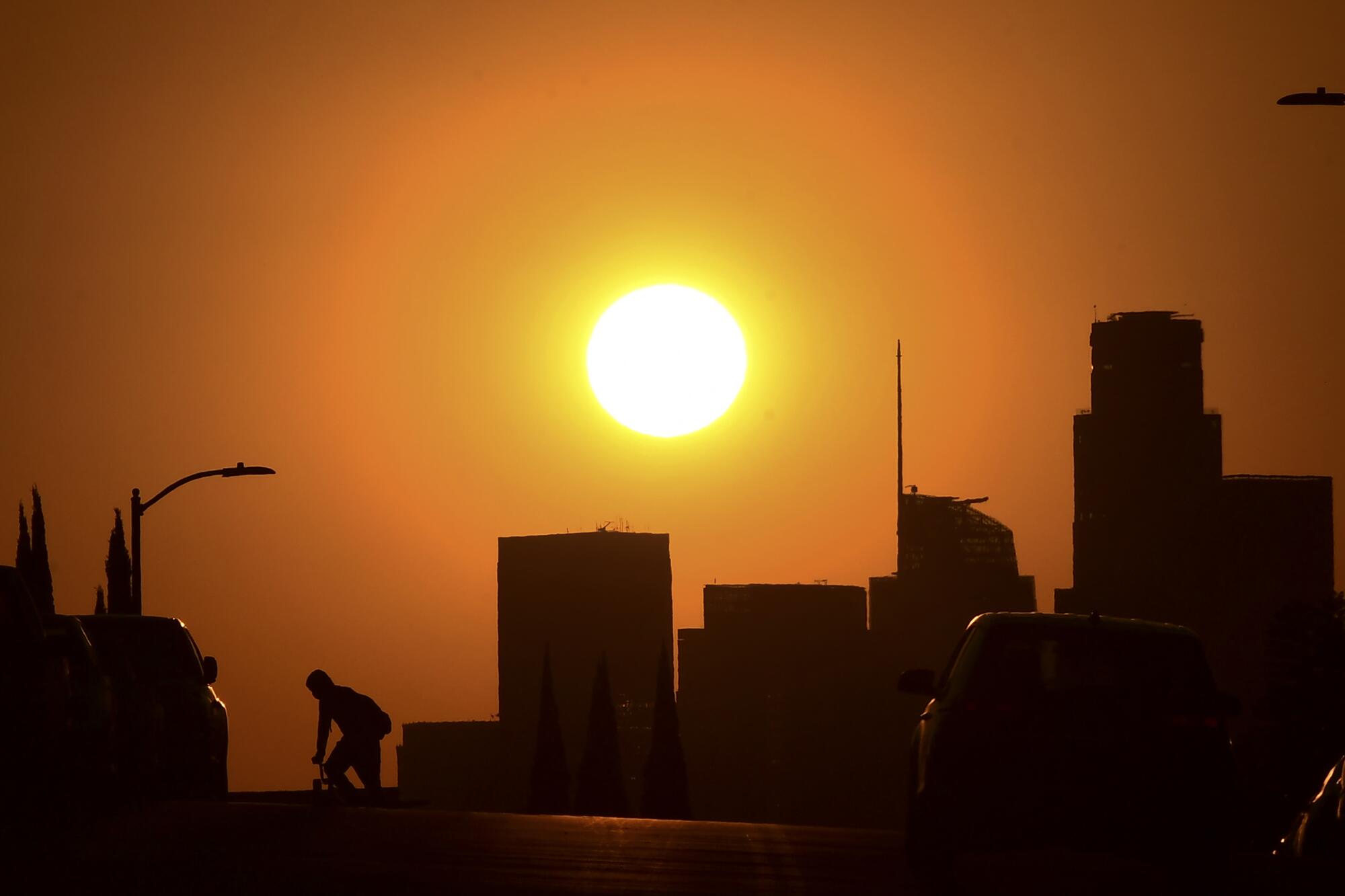 A bicyclist and the downtown Los Angeles skyline are silhouetted by the setting sun. 