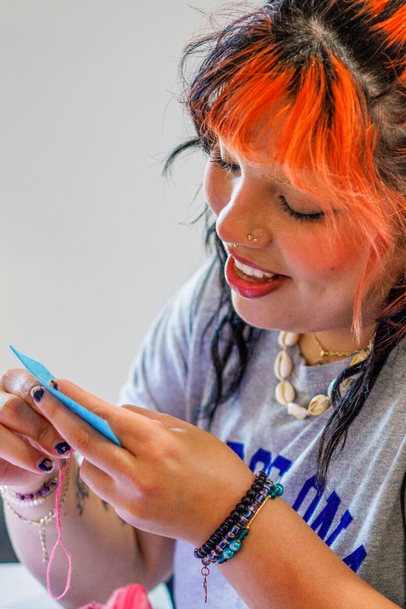 A person with dyed orange bangs works on a sewing design at the Radical Sewing Club.