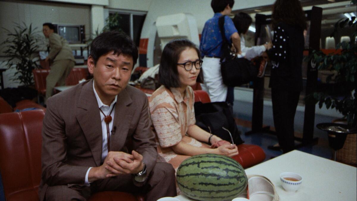 Two people with a watermelon wait in an office.