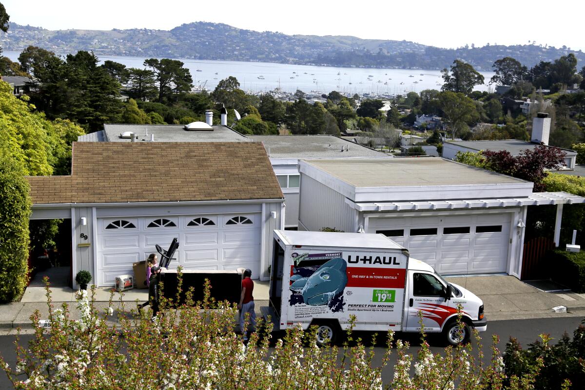 A U-Haul moving truck with people standing outside the white garage door of a home