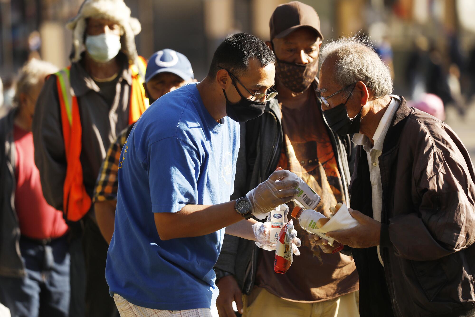 An elderly man receives food and drink from a masked volunteer in a line of people