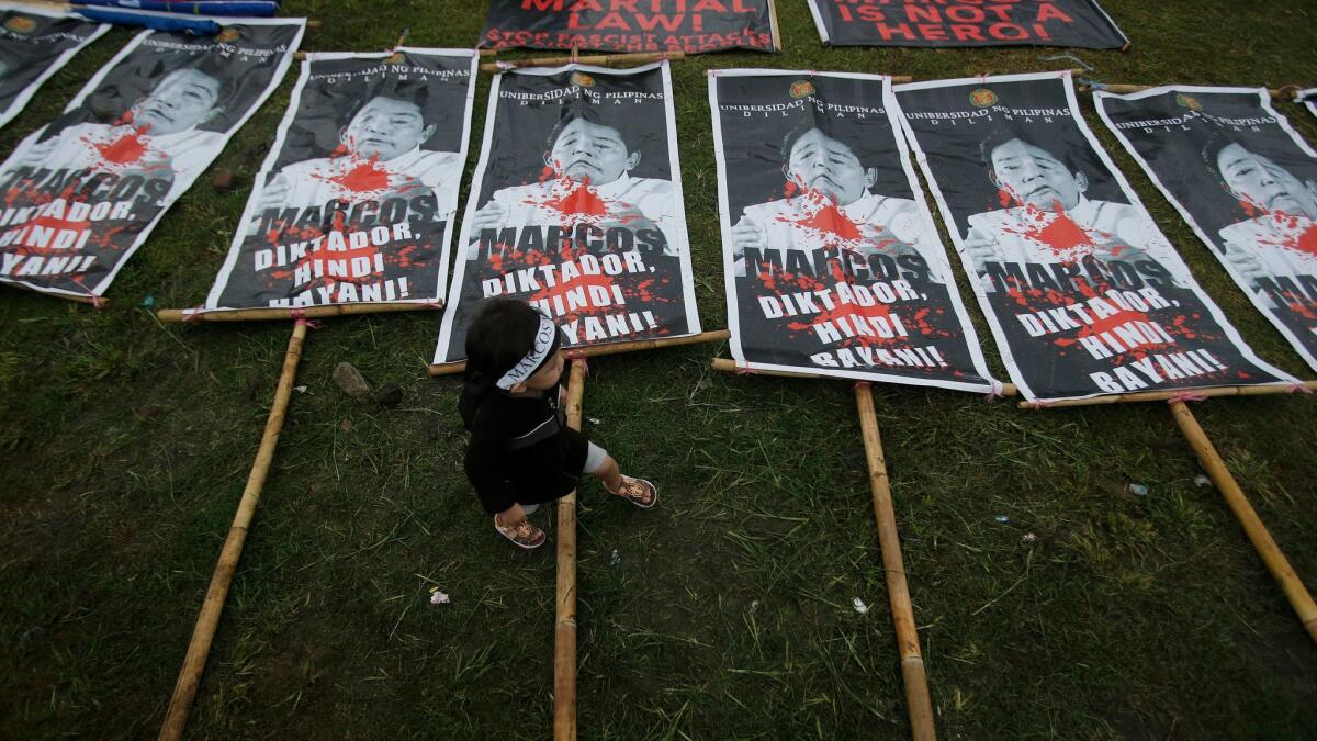 A Filipino boy walks beside posters with pictures of dictator Ferdinand Marcos during a rally Nov. 25 at Manila's Rizal Park.
