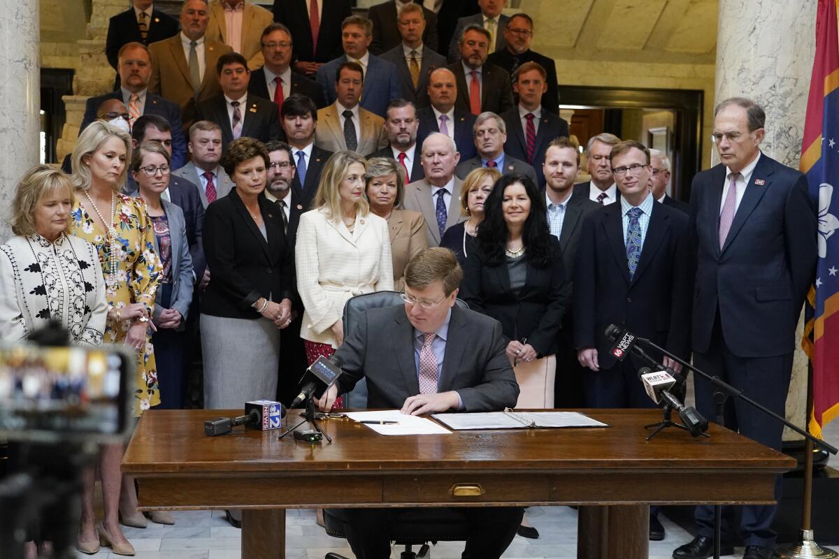 Mississippi Gov. Tate Reeves signs the first state bill in the U.S. this year to ban transgender athletes from competing on female sports teams, as supporting lawmakers gather behind him, Thursday, March 11, 2021, at the Capitol in Jackson, Miss. (AP Photo/Rogelio V. Solis)