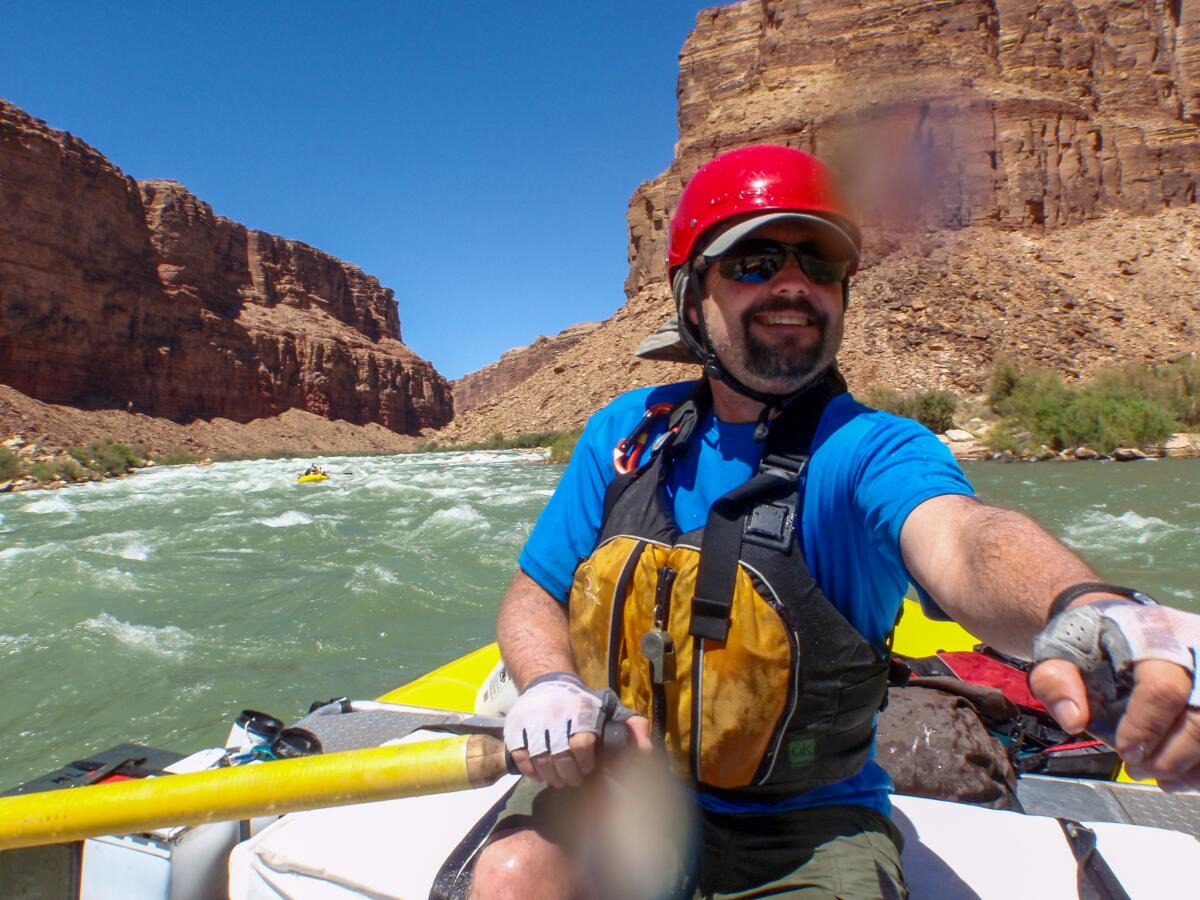 A man in a red helmet rows a raft through the Grand Canyon