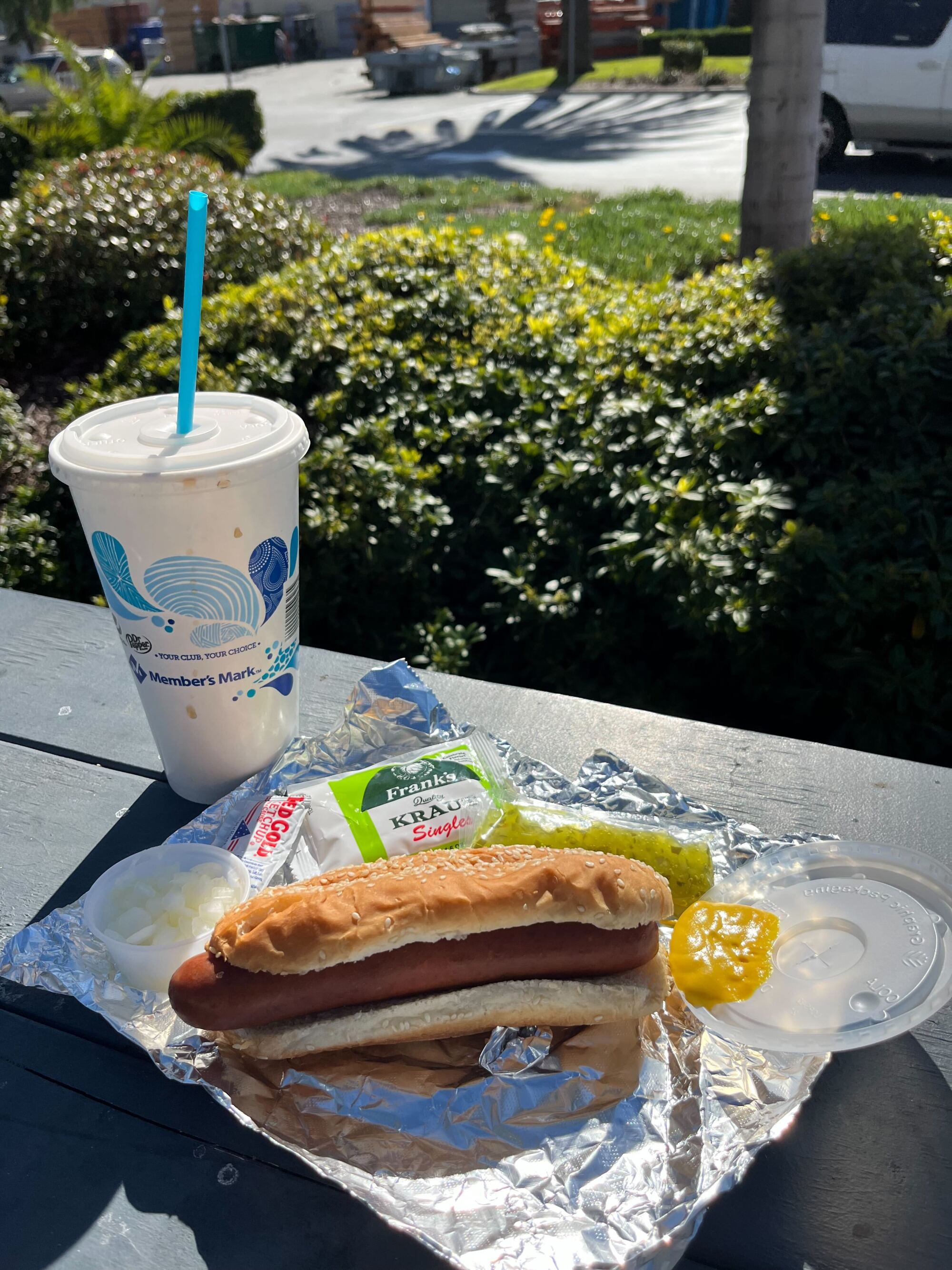 A hot dog and a drink outside on a picnic table 