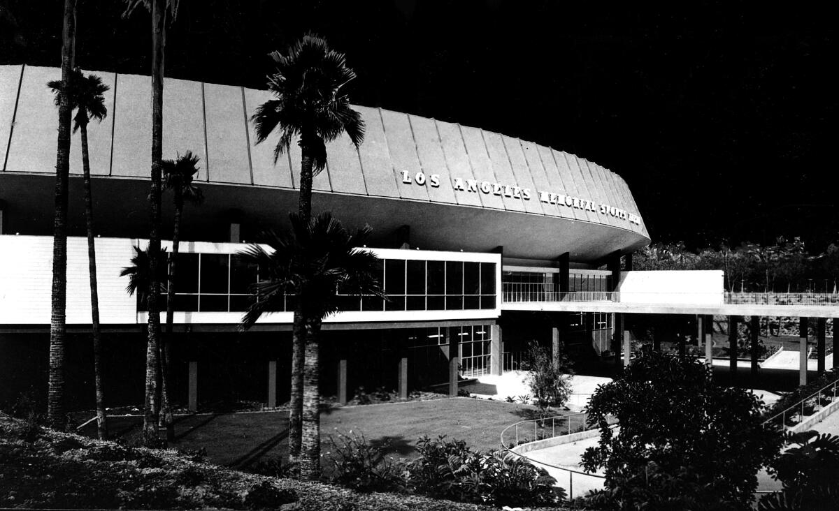 A black-and-white photo of a rounded building with palm trees.