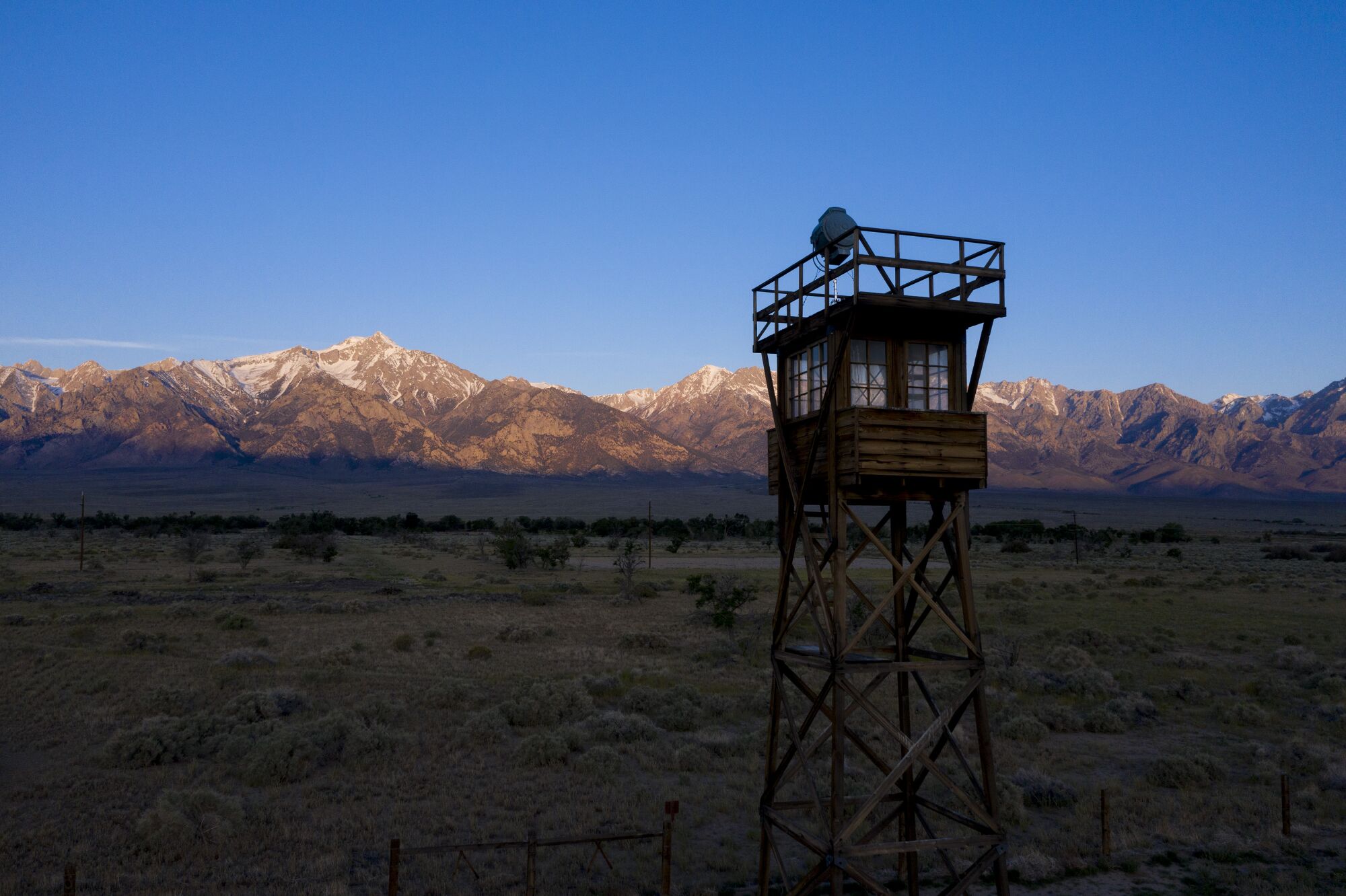 The rising sun illuminates the Sierra Nevada crest behind a restored guard tower at the Manzanar National Historic Site.